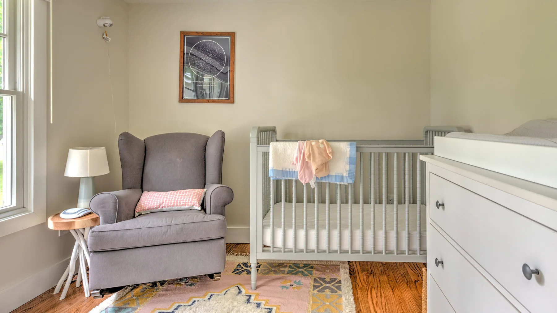 A nursery with a crib, an armchair, and a white dresser.