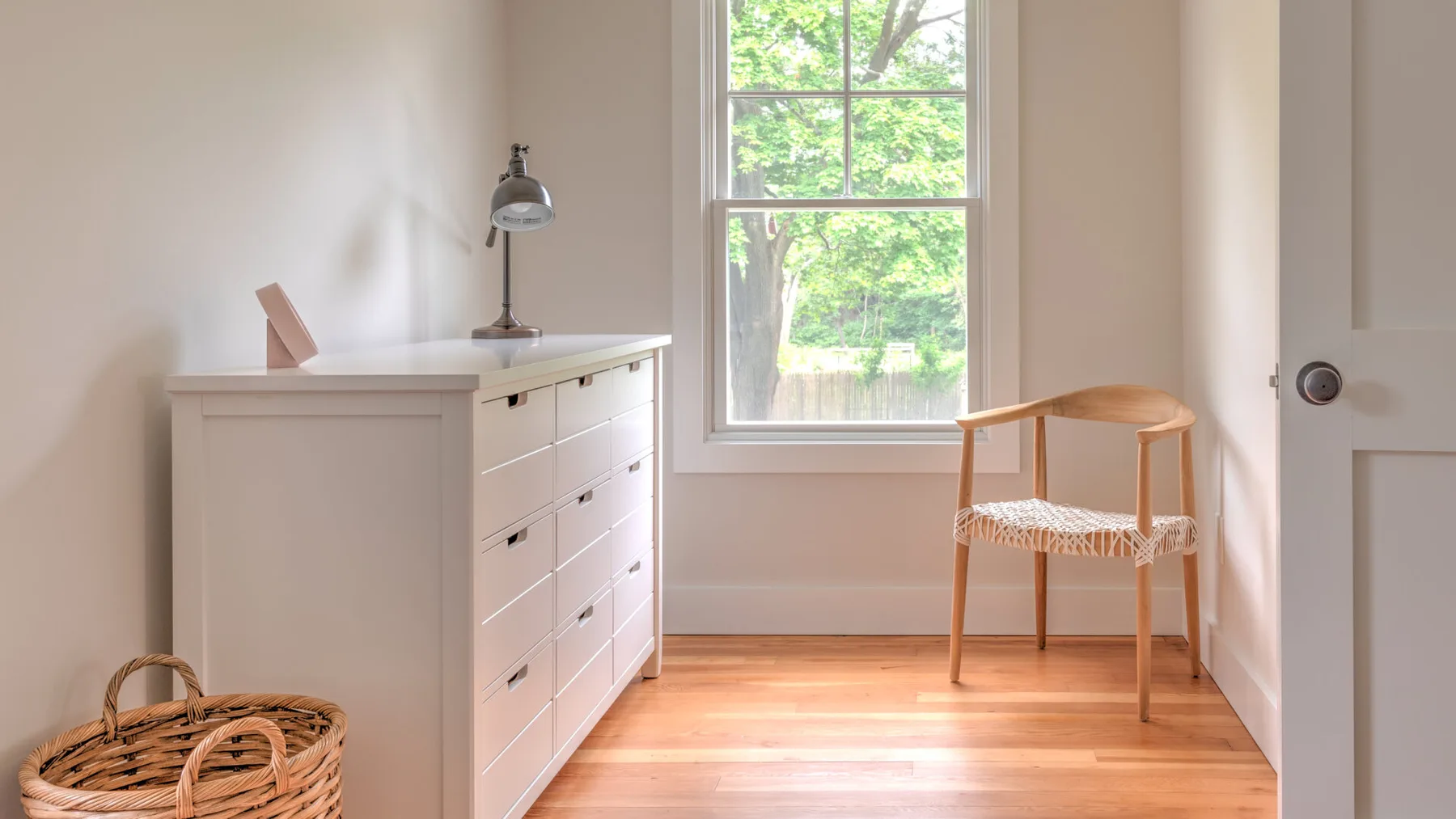 A bright room with a white desk, a window, and a wooden chair.