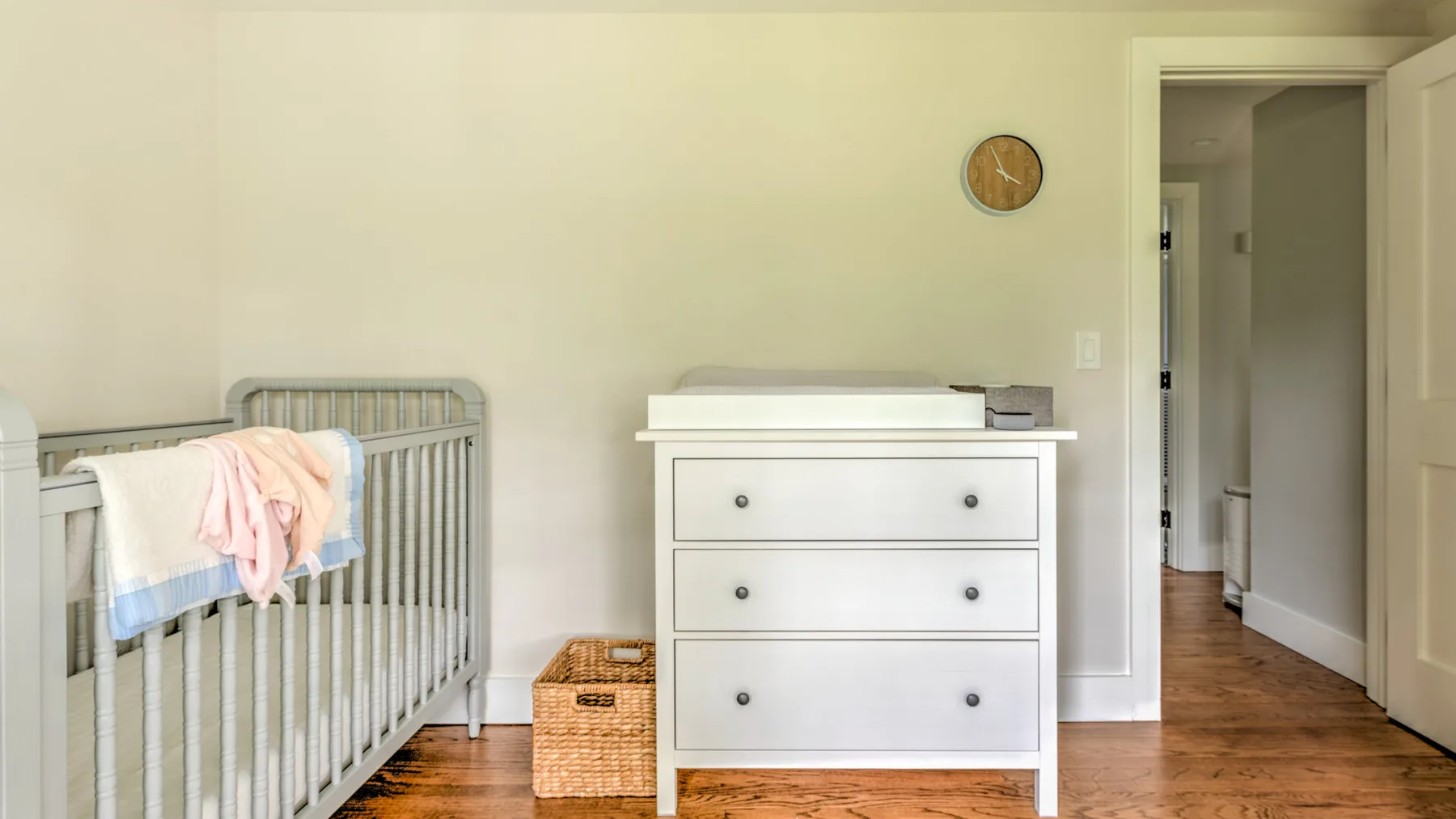 A nursery with a crib and white dresser beside an open doorway.