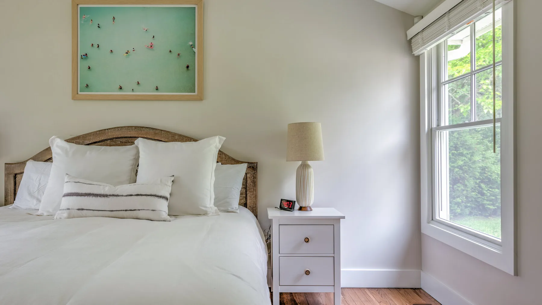 A bright bedroom with a neatly made bed beside a large window.