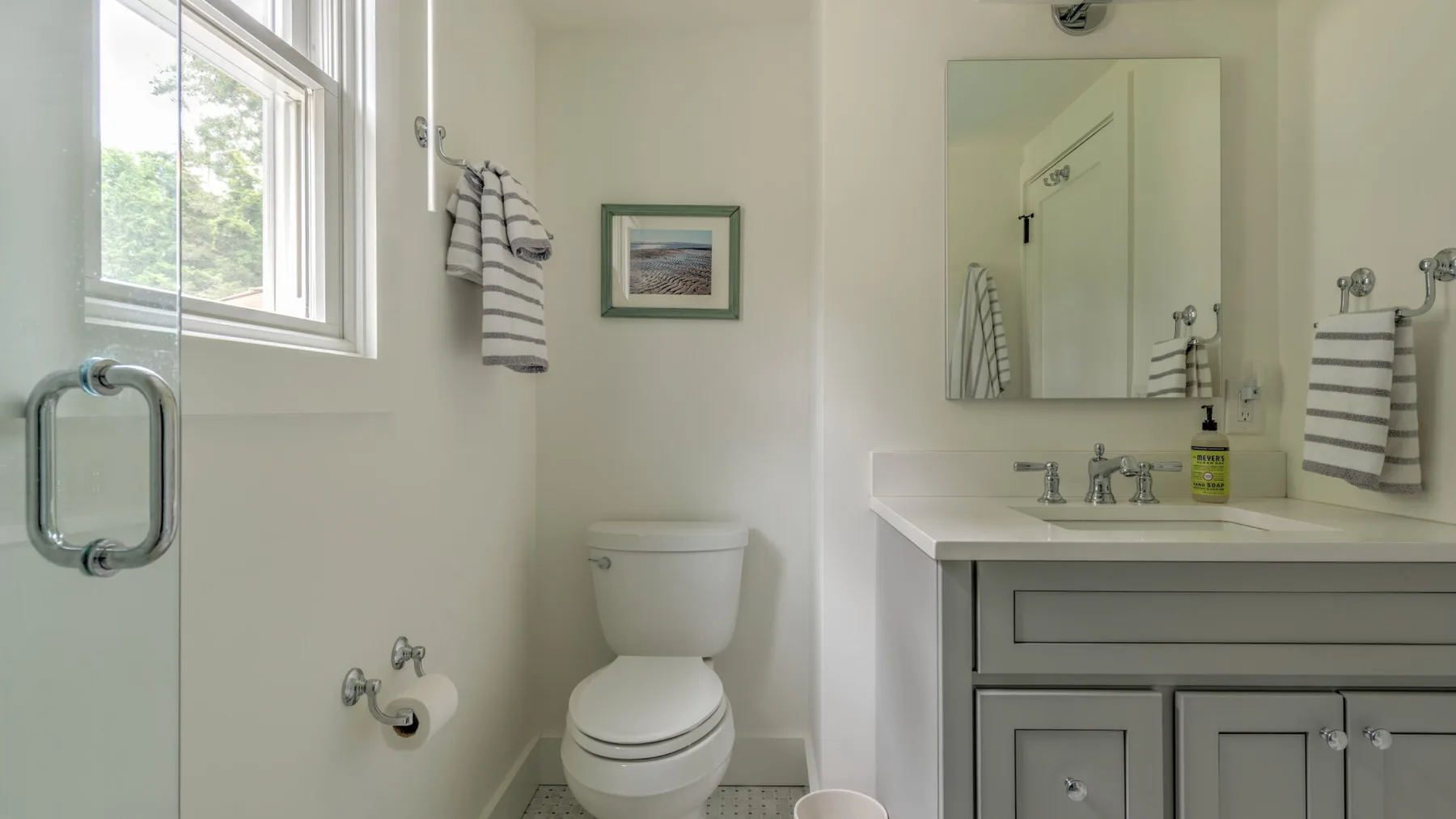 A bright bathroom with a toilet, vanity, and window.