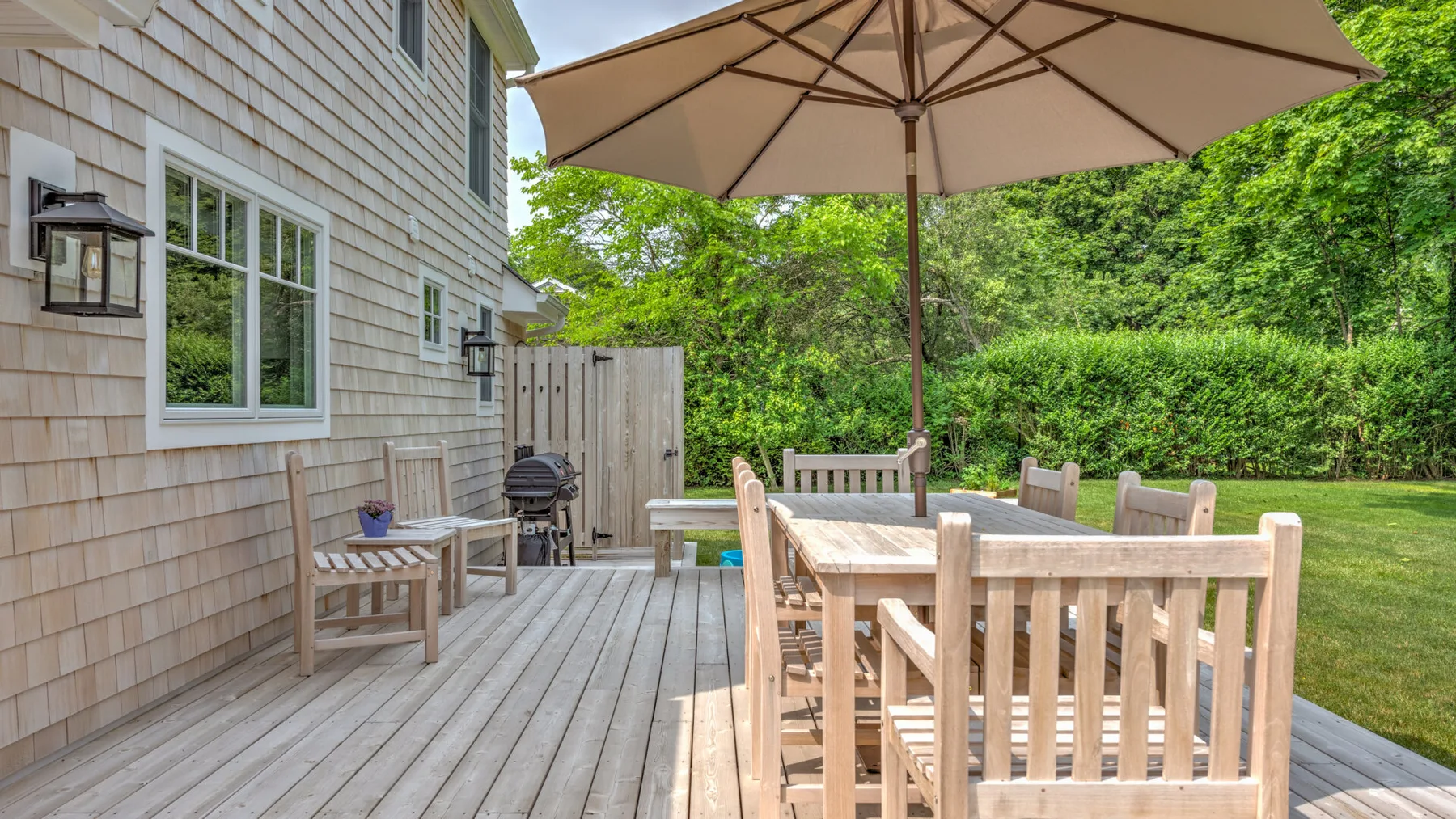 An outdoor deck dining area with a wooden table and a large umbrella.