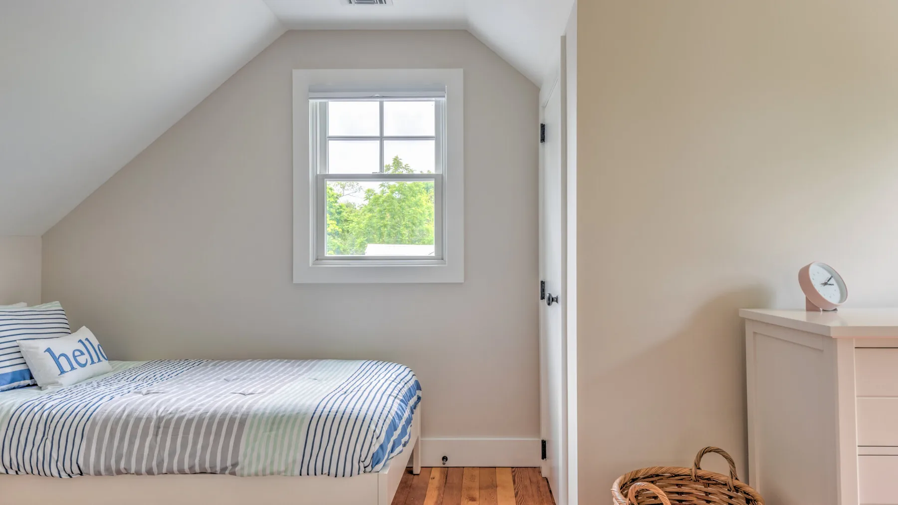 A bedroom with a bed beneath a window and a dresser nearby.