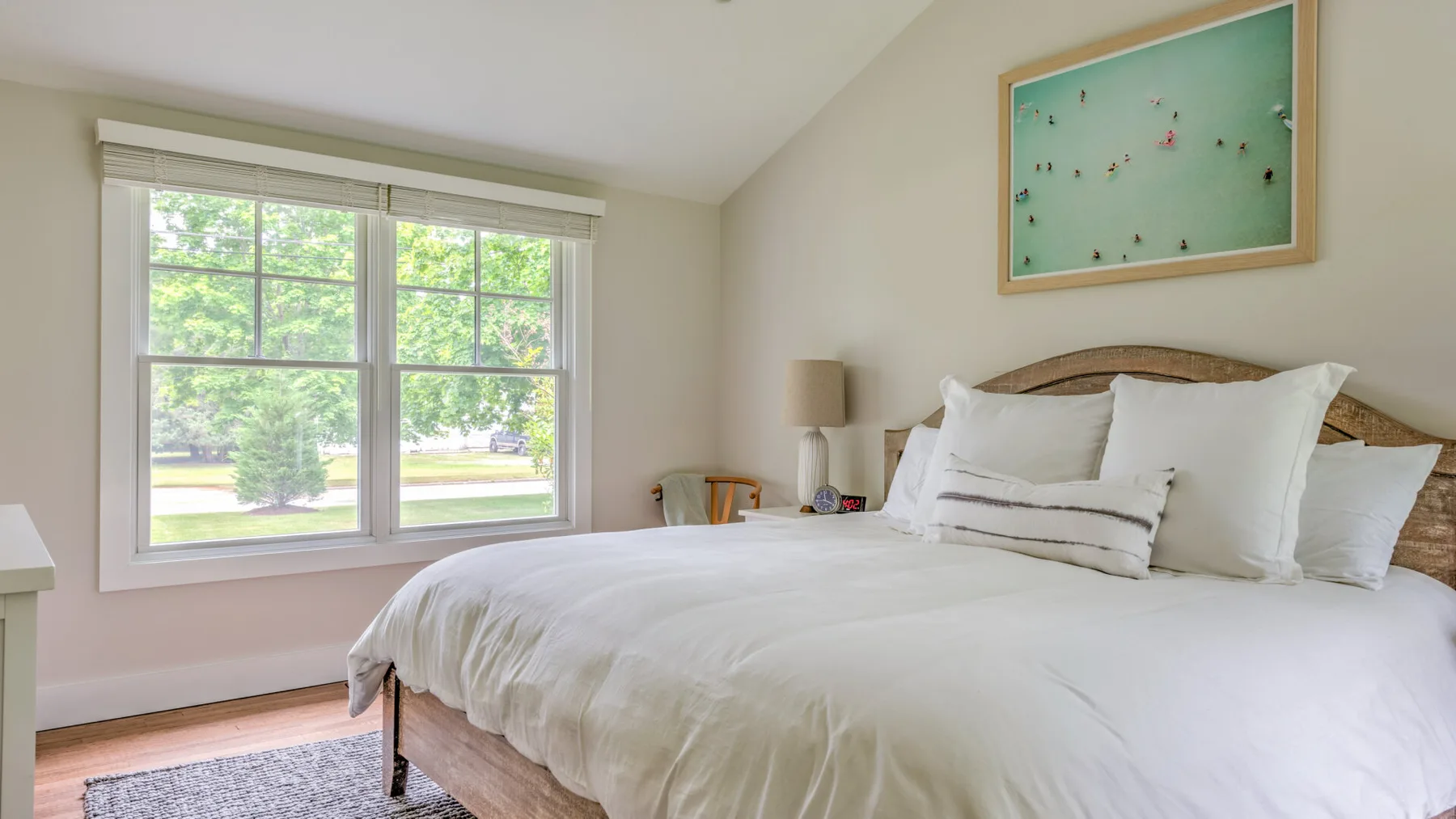 A bright bedroom with a large bed and a window overlooking greenery.