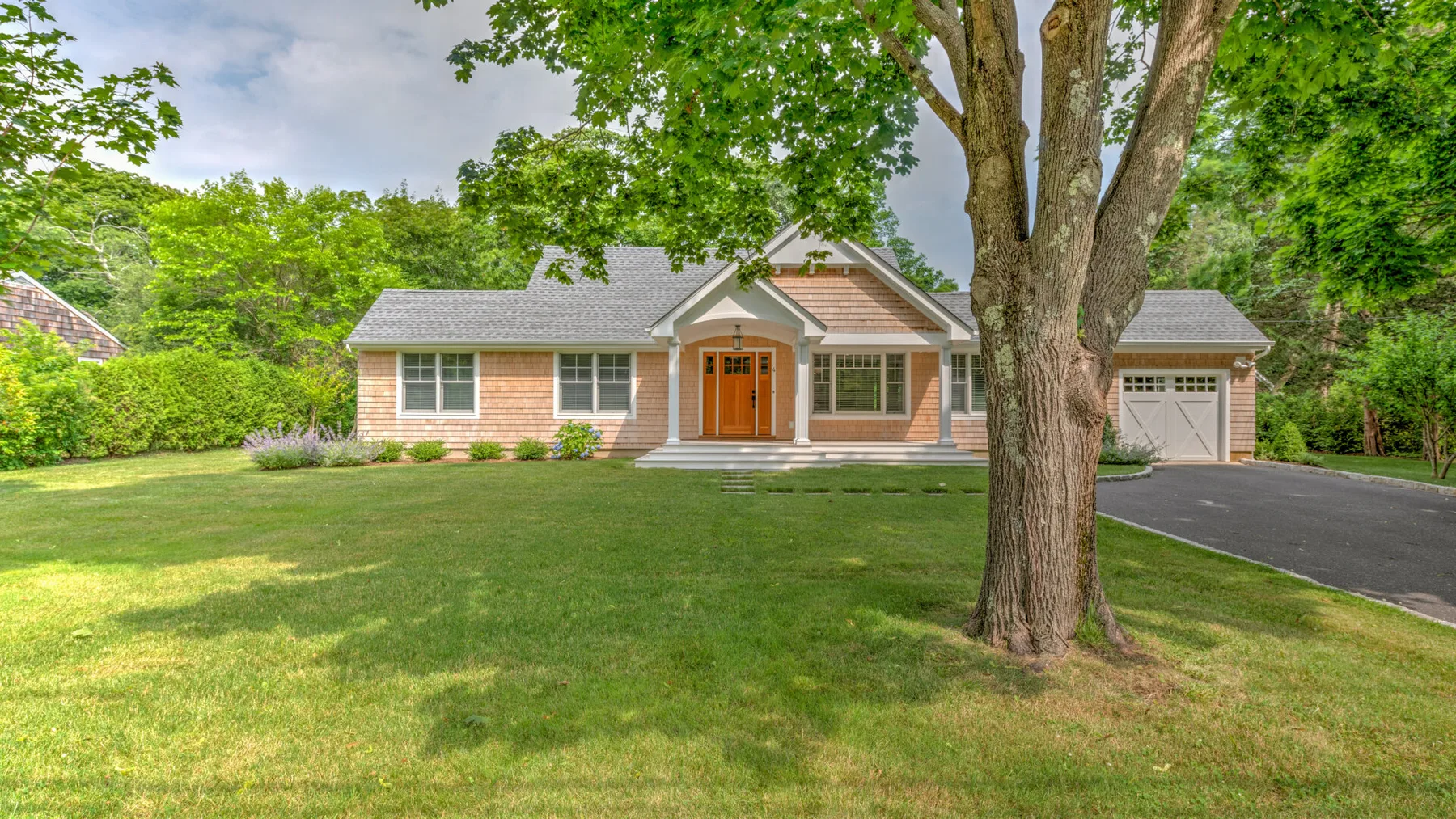 A brick house faces a broad green lawn, with mature trees around the front yard.