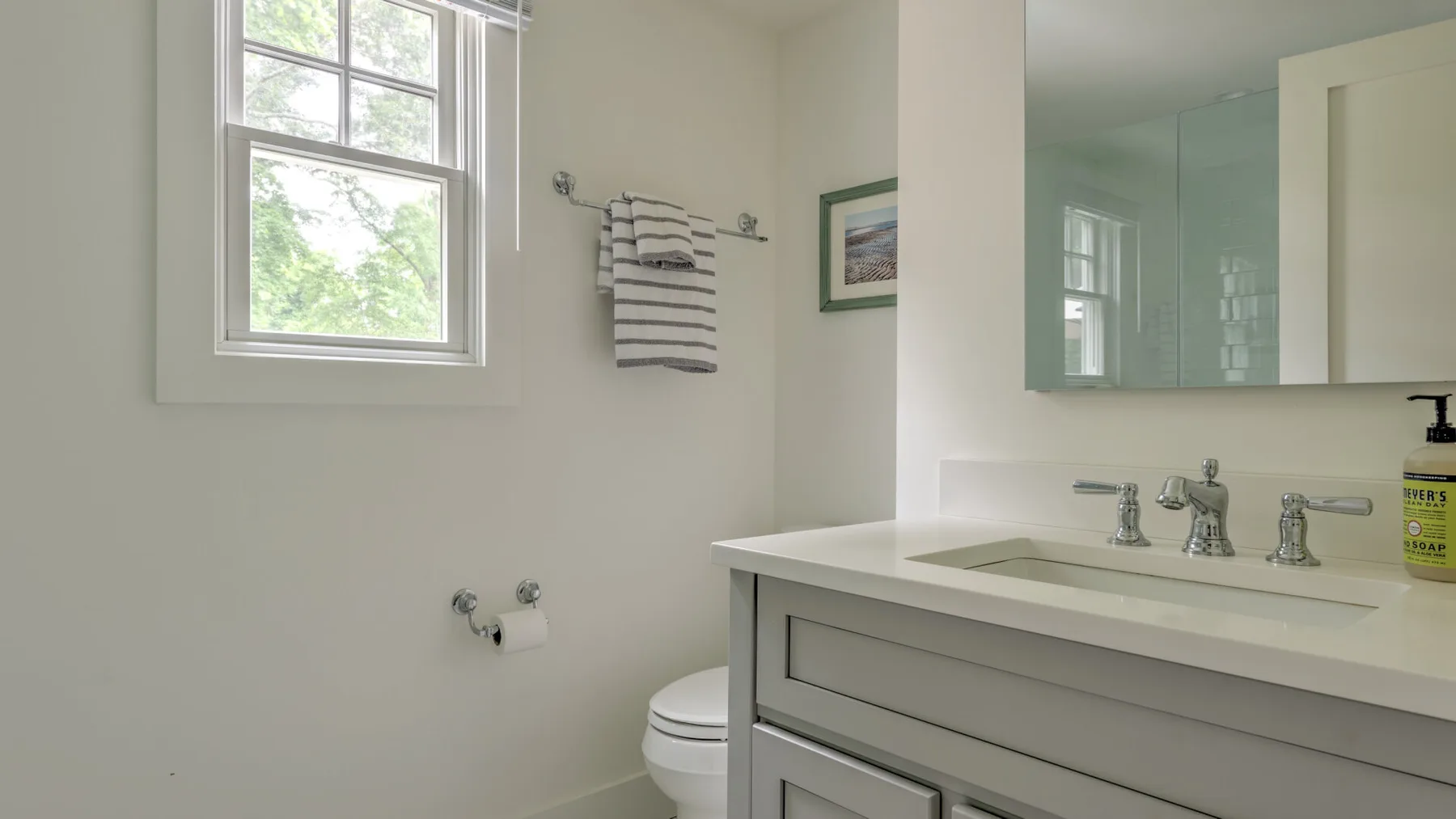 A bright bathroom with a vanity, mirrored cabinet, toilet, and window.