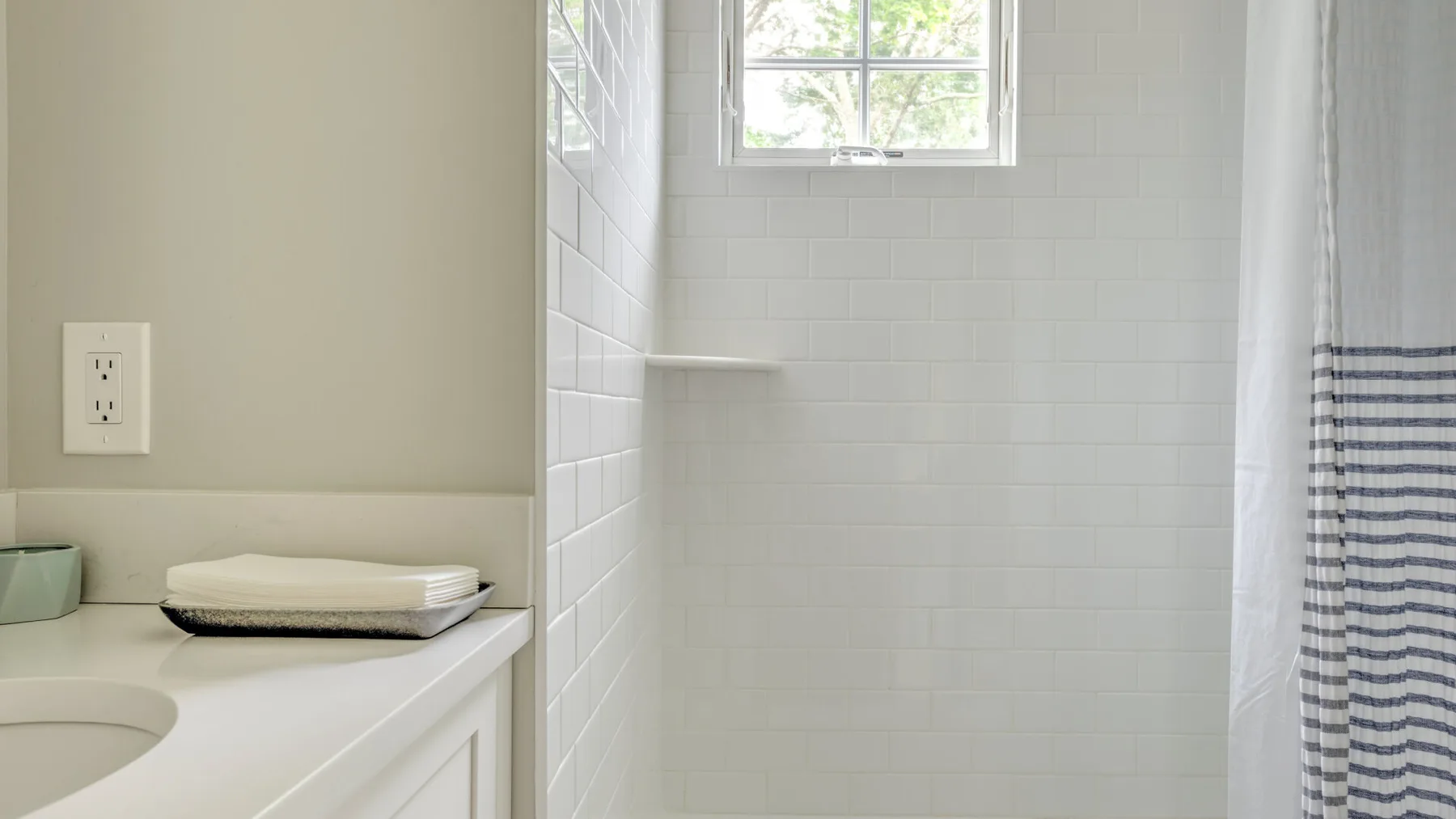 A bathroom vanity with a sink sits beside a tiled shower with a striped curtain.