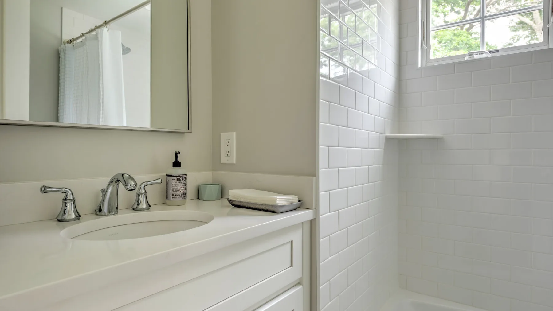 A bright bathroom with a sink, mirror, and tiled shower.