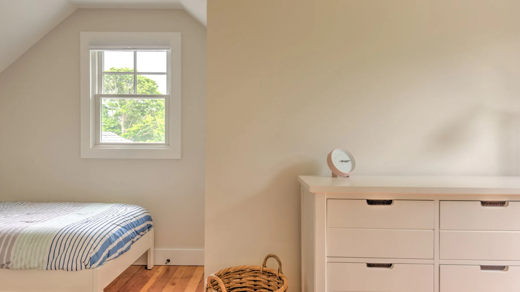 A bedroom with a bed beside a dresser and a window.
