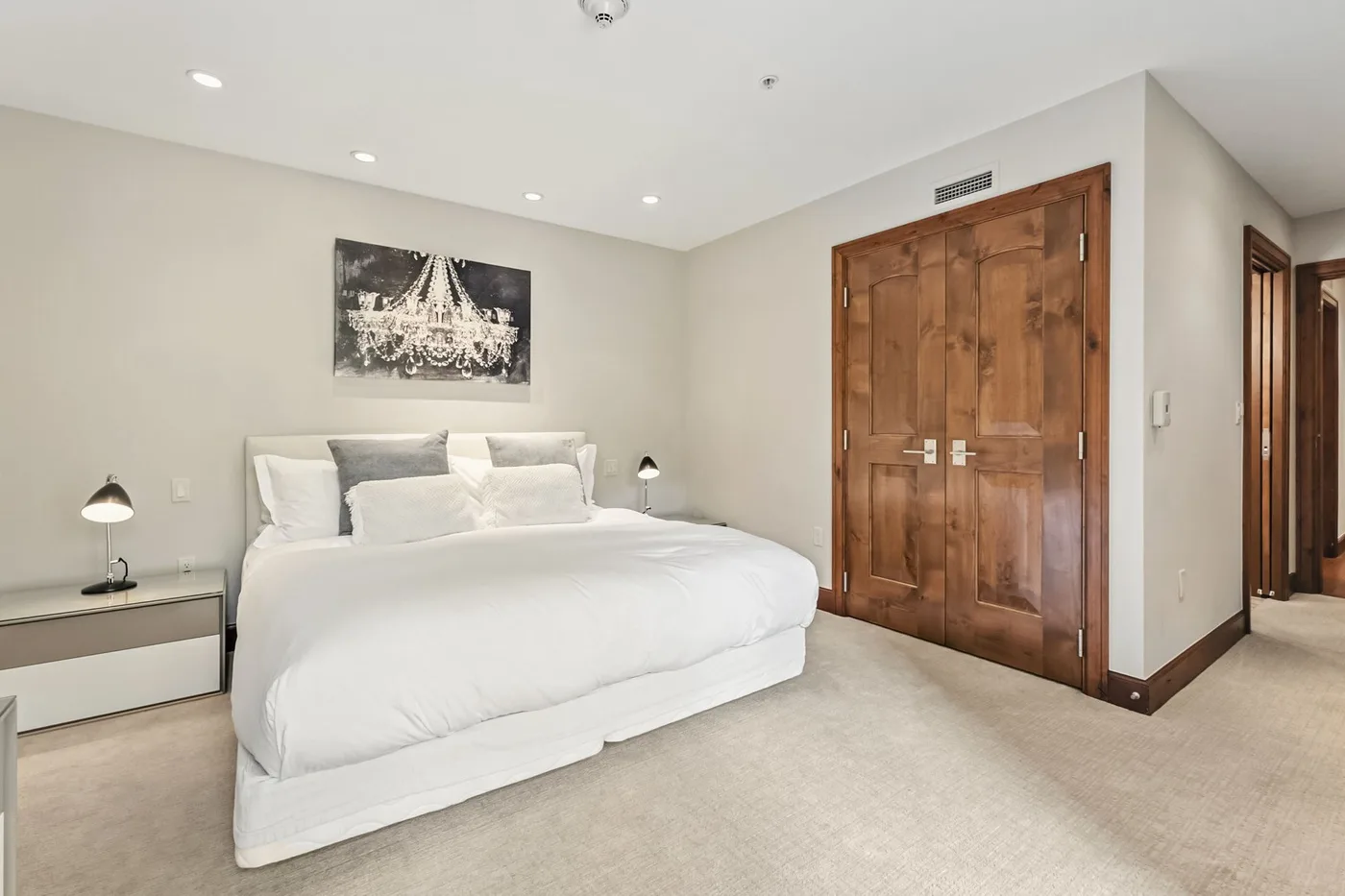 A bright bedroom with a neatly made bed and wooden double doors.