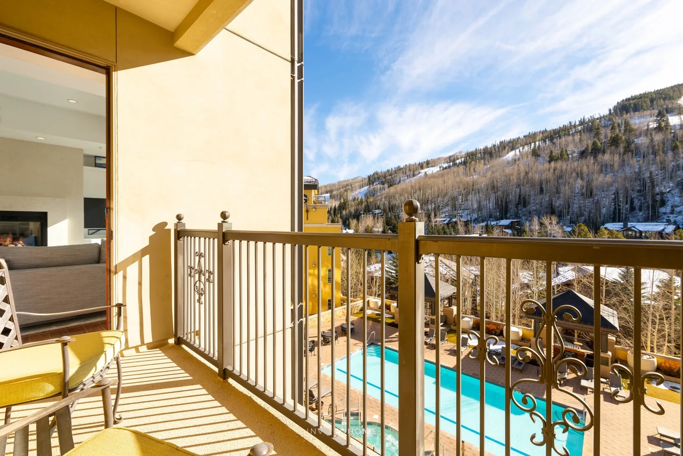 A balcony overlooks an outdoor pool and a wooded hillside.