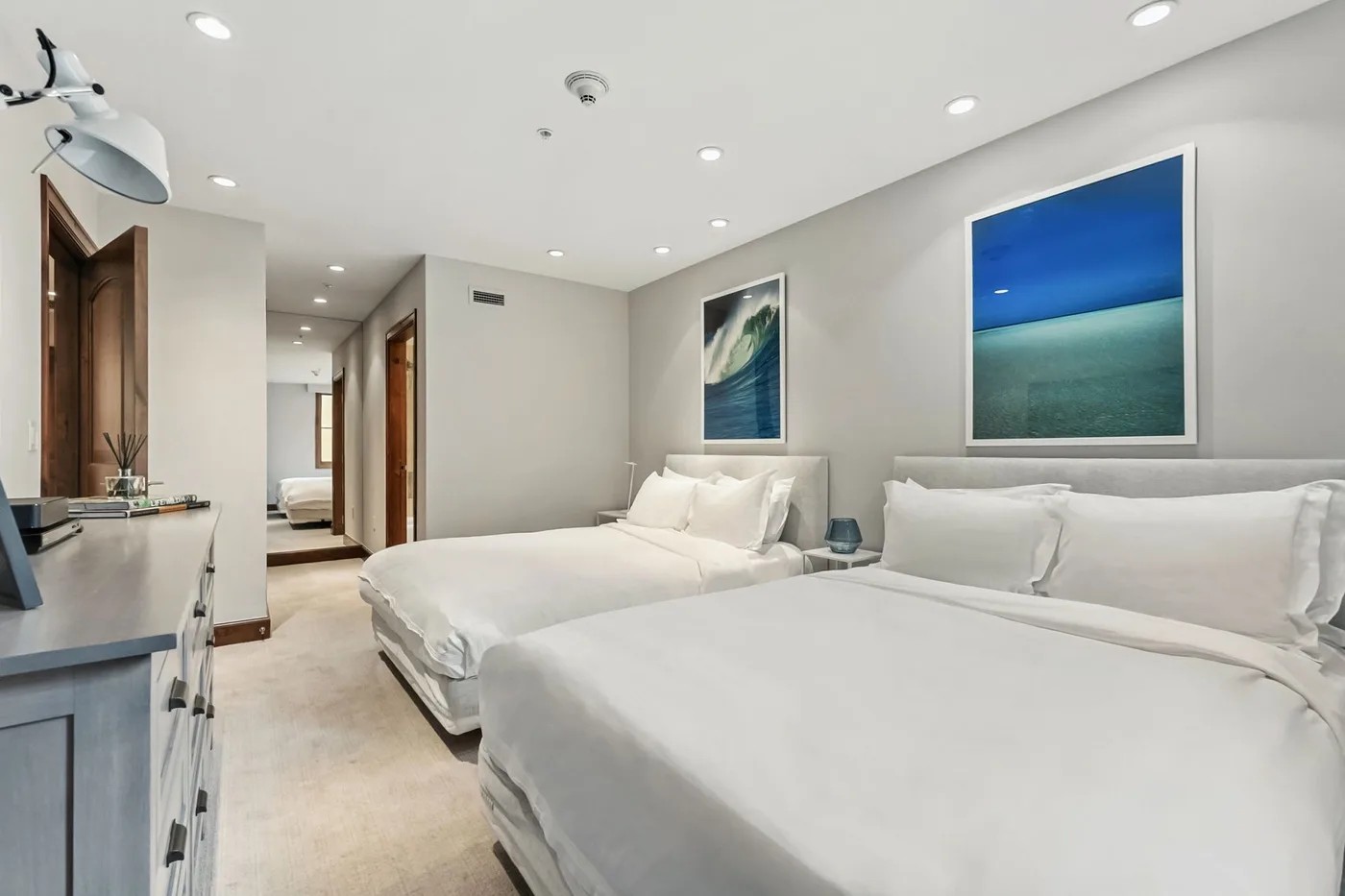 A bedroom with two beds and framed ocean artwork on the walls.