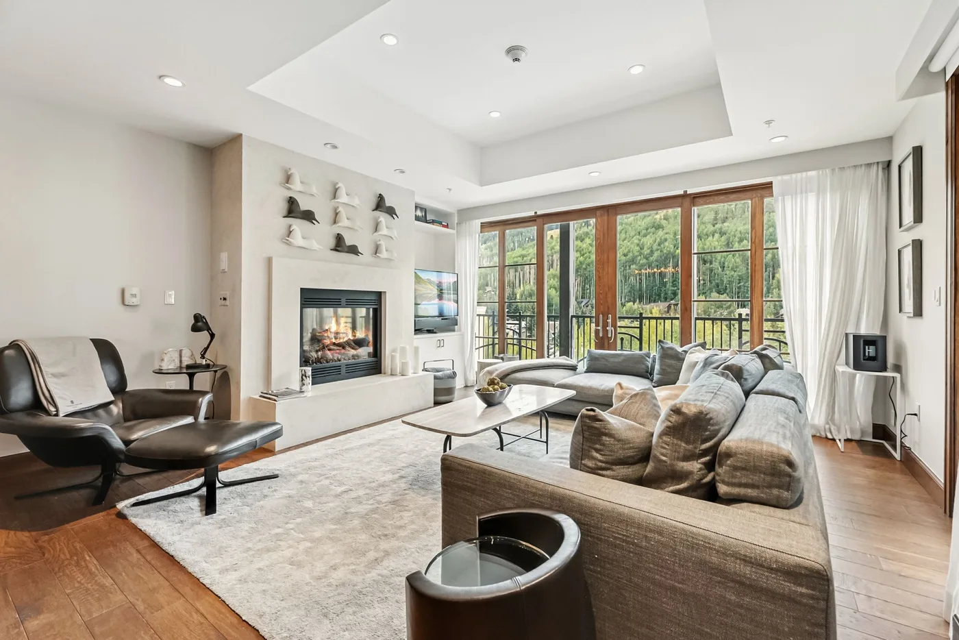 A bright living room with seating around a fireplace and large windows.