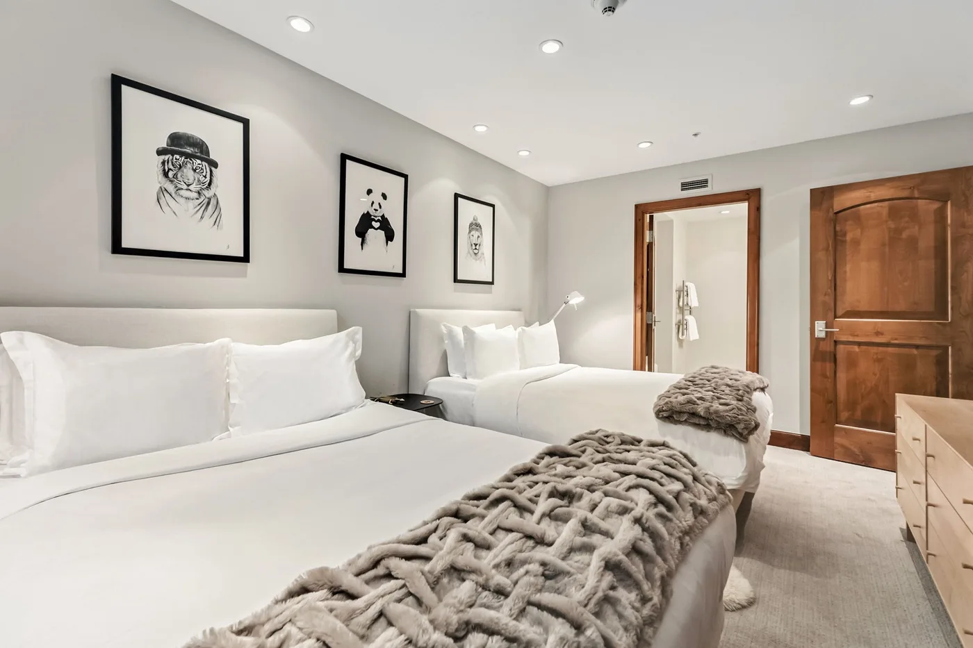 A bright bedroom with two beds, framed artwork, and wooden doors.