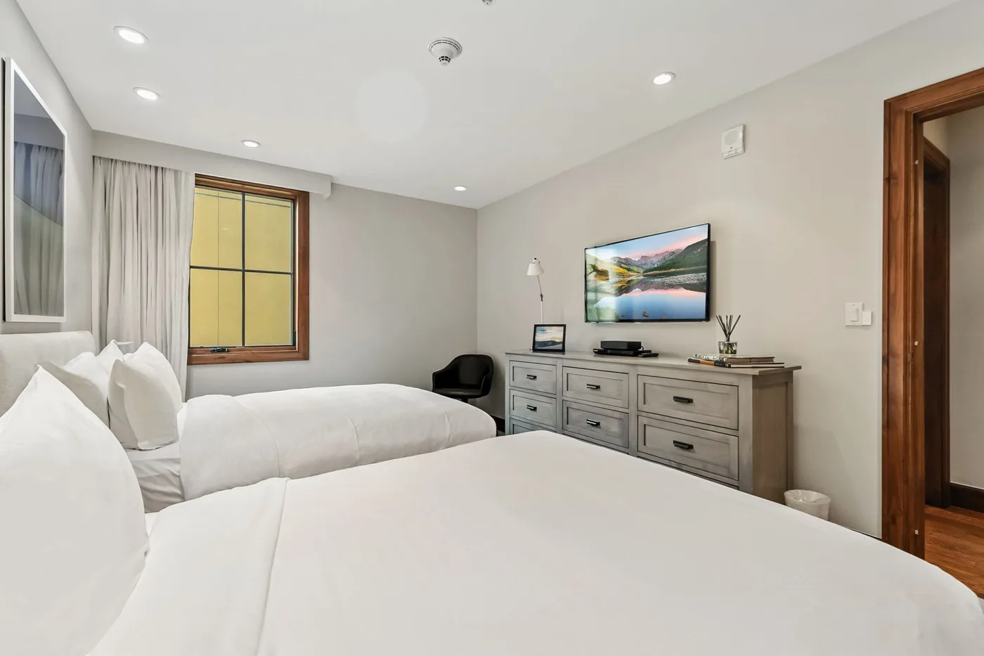 A bedroom with two beds and a dresser beneath a wall-mounted television.
