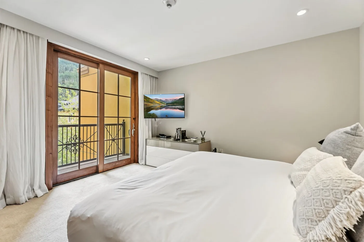 A bright bedroom with a neatly made bed and glass doors opening onto a balcony.