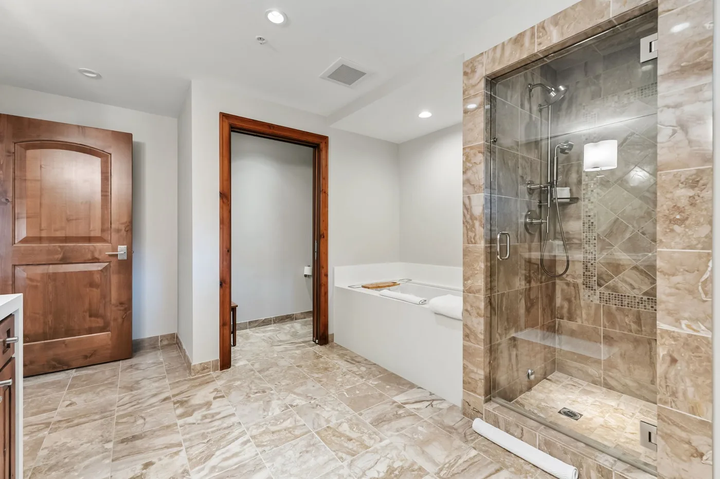 A tiled bathroom with a glass shower and a bathtub beside the doorway.