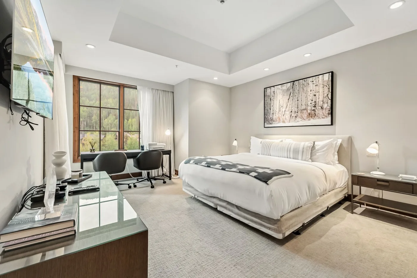 A bright bedroom with a large bed, bedside tables, and a window-side desk.