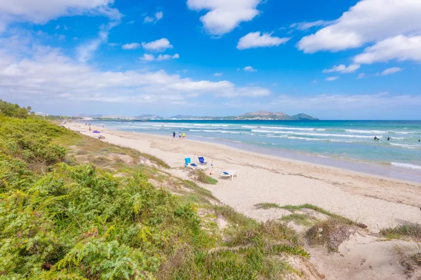 Una playa de arena se extiende junto al mar bajo un cielo parcialmente nublado.