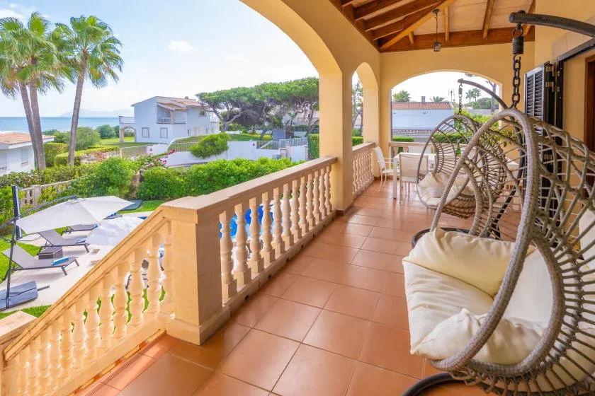 Una terraza cubierta da a una piscina, con sillones colgantes acolchados cerca.