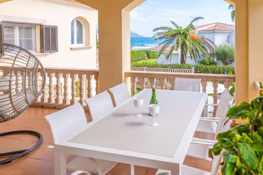 Una terraza cubierta con una mesa blanca, palmeras y vistas al mar.