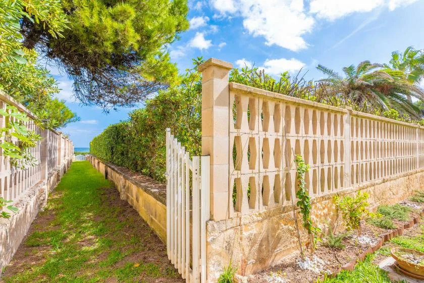 Un estrecho sendero de jardín bordea una cerca decorativa y vegetación.