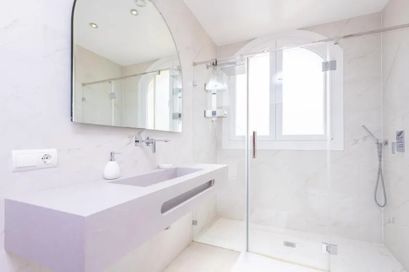 Un baño luminoso con una encimera larga y una ducha de cristal.
