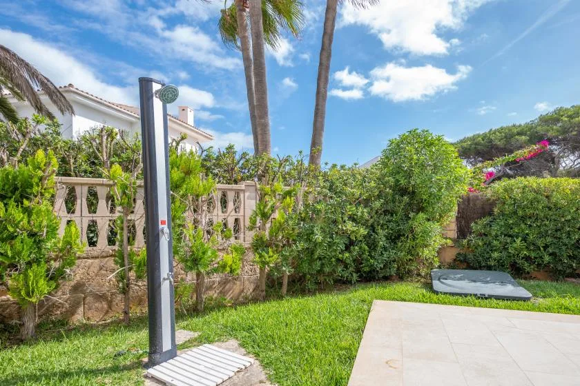 Un patio ajardinado con una ducha exterior independiente junto a setos verdes.