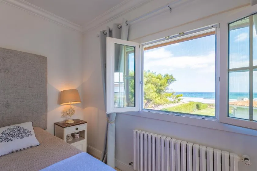 Un dormitorio con una cama junto a ventanas abiertas con vistas al mar.