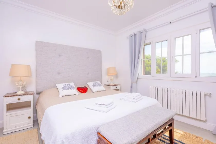 Un dormitorio luminoso con una cama bien hecha y ventanas grandes.
