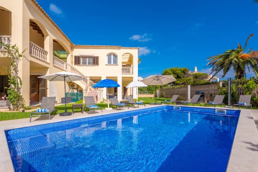 Una piscina junto a una villa, con asientos de patio y sombrillas.