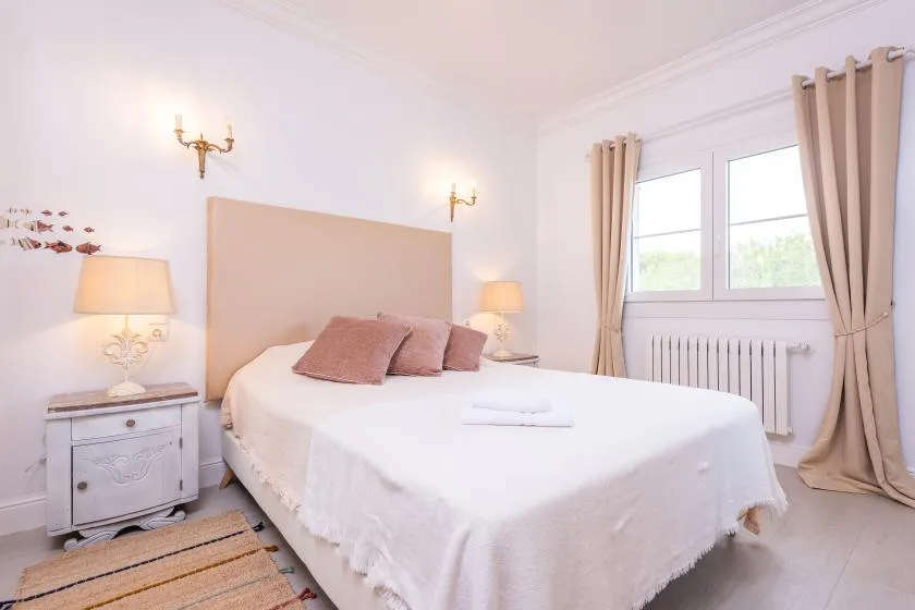 Un dormitorio luminoso con una cama bien hecha y una ventana grande.