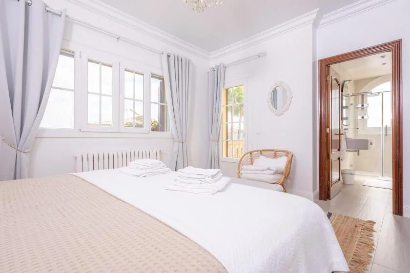 Un dormitorio luminoso con una cama bien hecha y ventanas grandes.