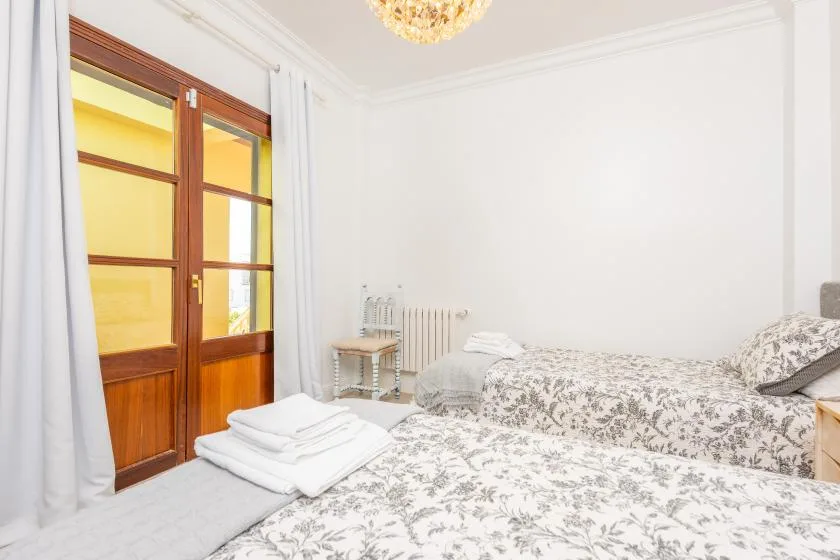 Dormitorio con ropa de cama estampada, toallas dobladas y una puerta de madera con paneles de vidrio.