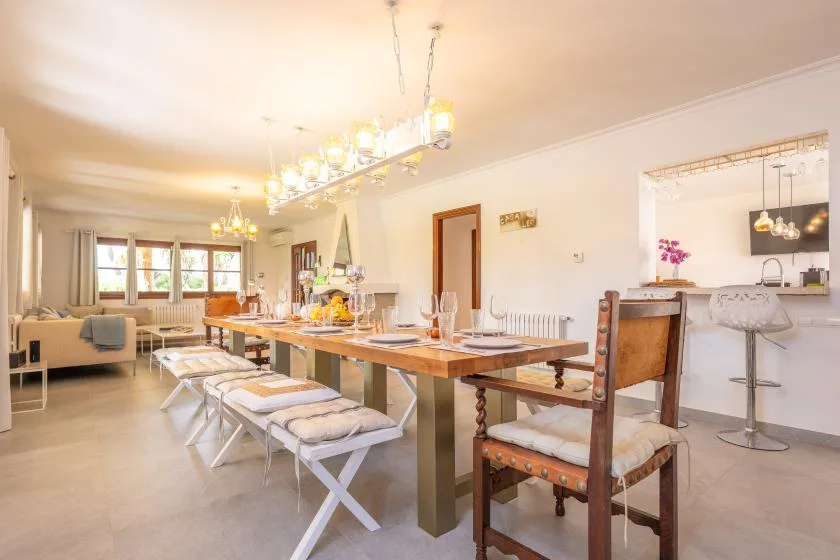 Un comedor luminoso con una larga mesa de madera y una cocina abierta al fondo.