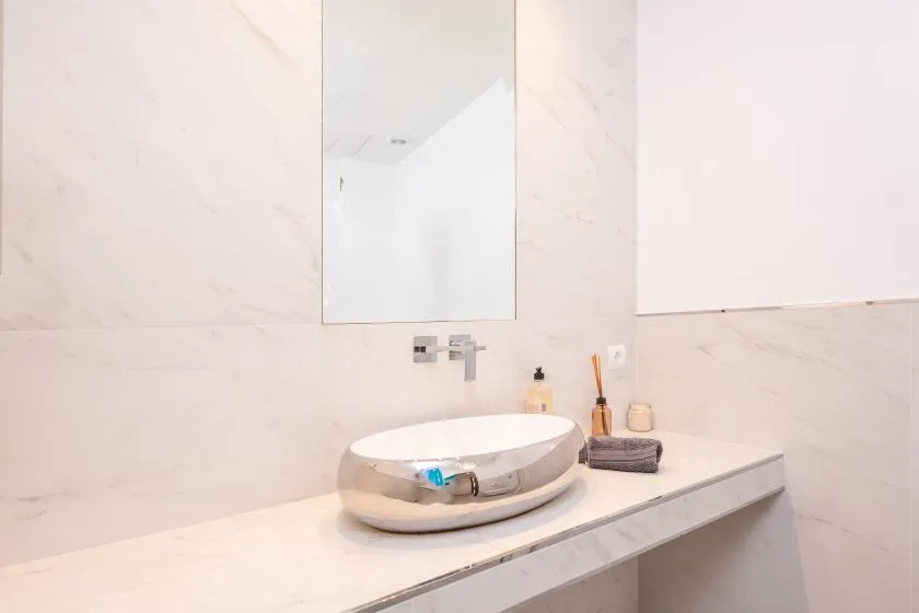 Un tocador de baño con lavabo sobrepuesto, espejo y artículos de aseo.