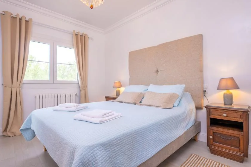 Un dormitorio luminoso con una cama arreglada y ventanas con cortinas.