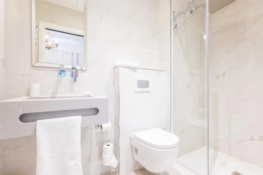 Un baño luminoso con lavabo suspendido, inodoro de pared y ducha de cristal.