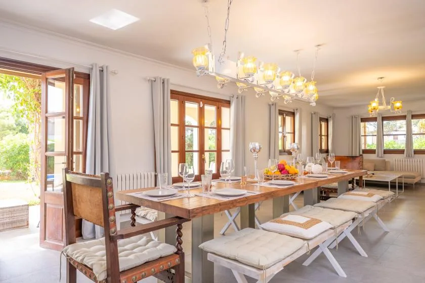 Una mesa larga está puesta bajo lámparas colgantes en un comedor luminoso.