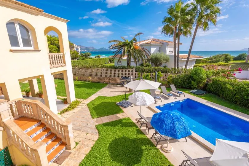 Patio de una villa junto al mar con piscina, asientos y palmeras.