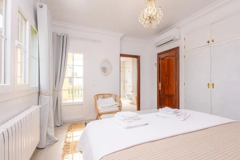 Un dormitorio luminoso con una cama bien hecha, ventanas altas y armarios empotrados blancos.