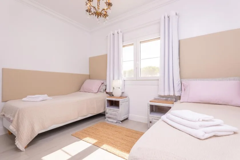 Un dormitorio luminoso con dos camas, una ventana y cortinas claras.