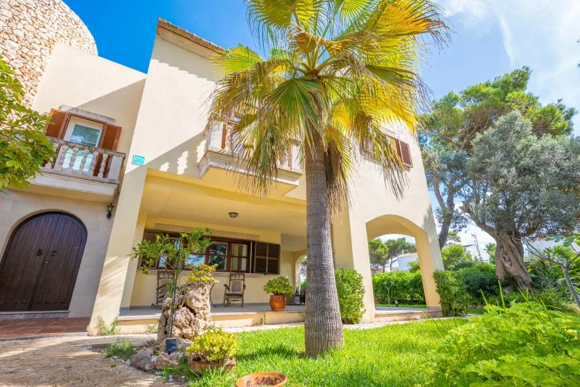 Una casa de estuco con una palmera en el jardín delantero soleado.