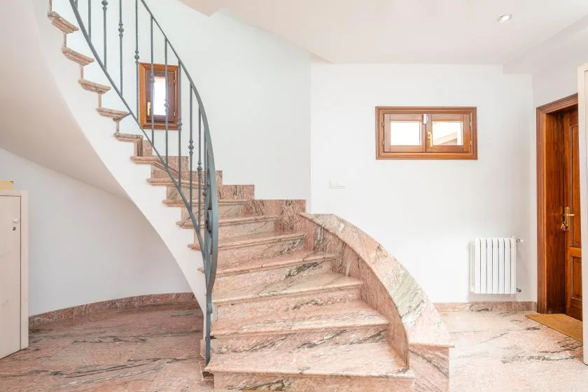 Escalera interior con peldaños curvos de piedra y una barandilla metálica oscura.