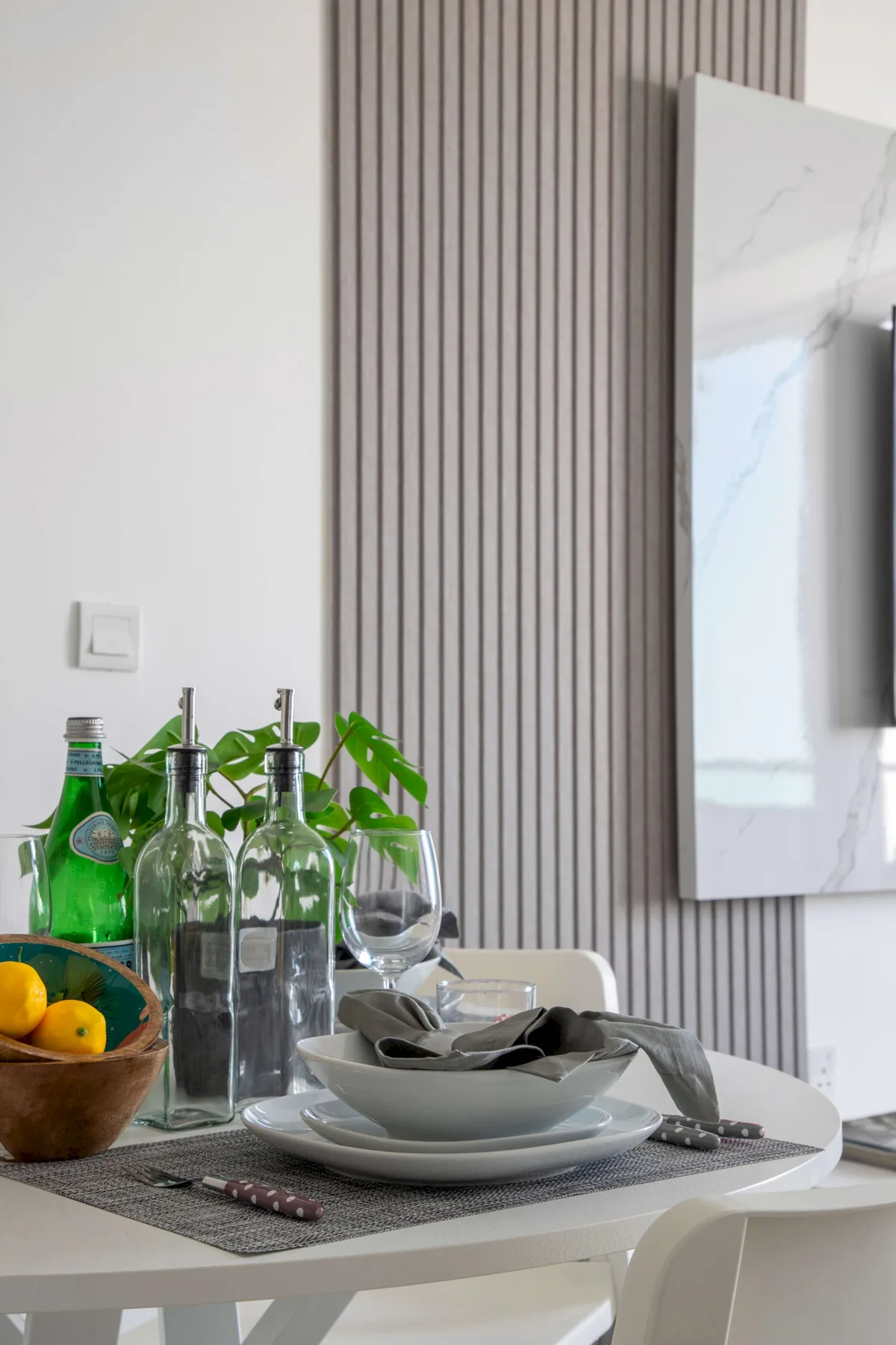 Dining table with place settings and glass bottles beside a ribbed wall.