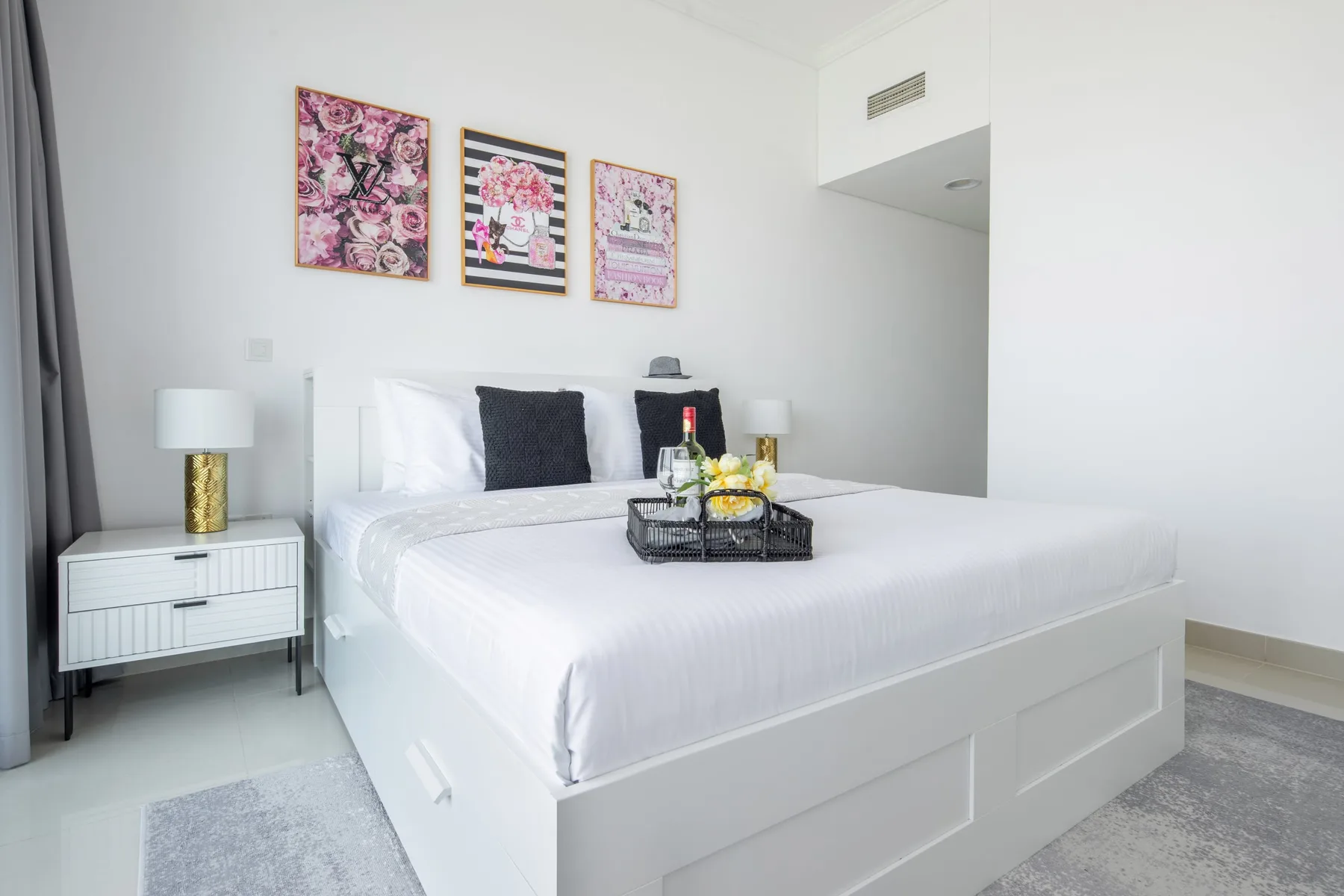 A bright bedroom with a white bed and three framed artworks above it.