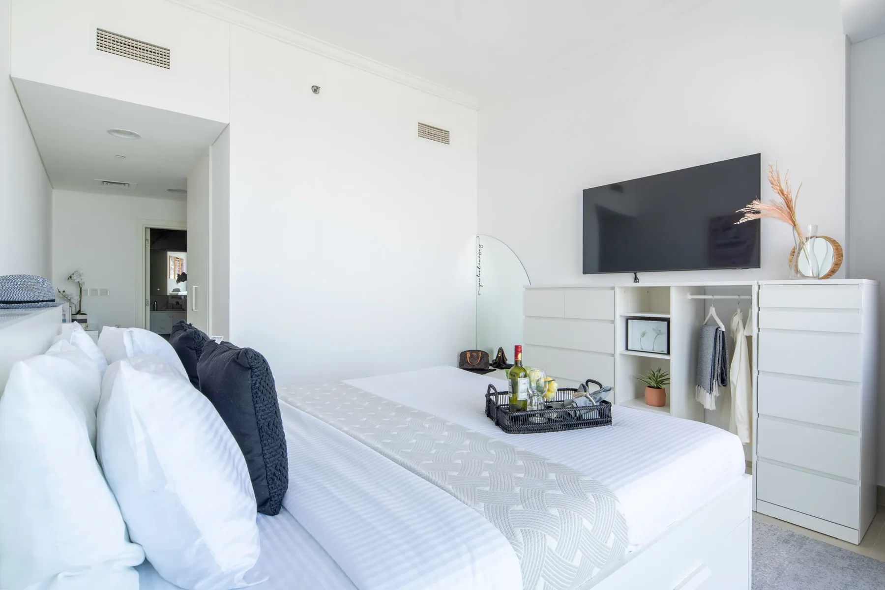 A bright bedroom with a neatly made bed and a wall-mounted television.