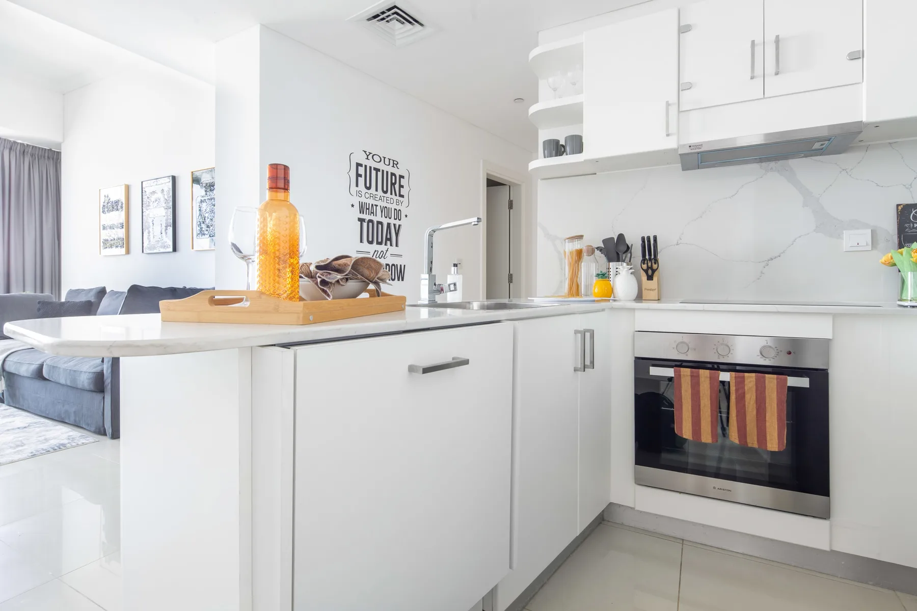 A bright modern kitchen with white cabinets and a countertop overlooking a living area.