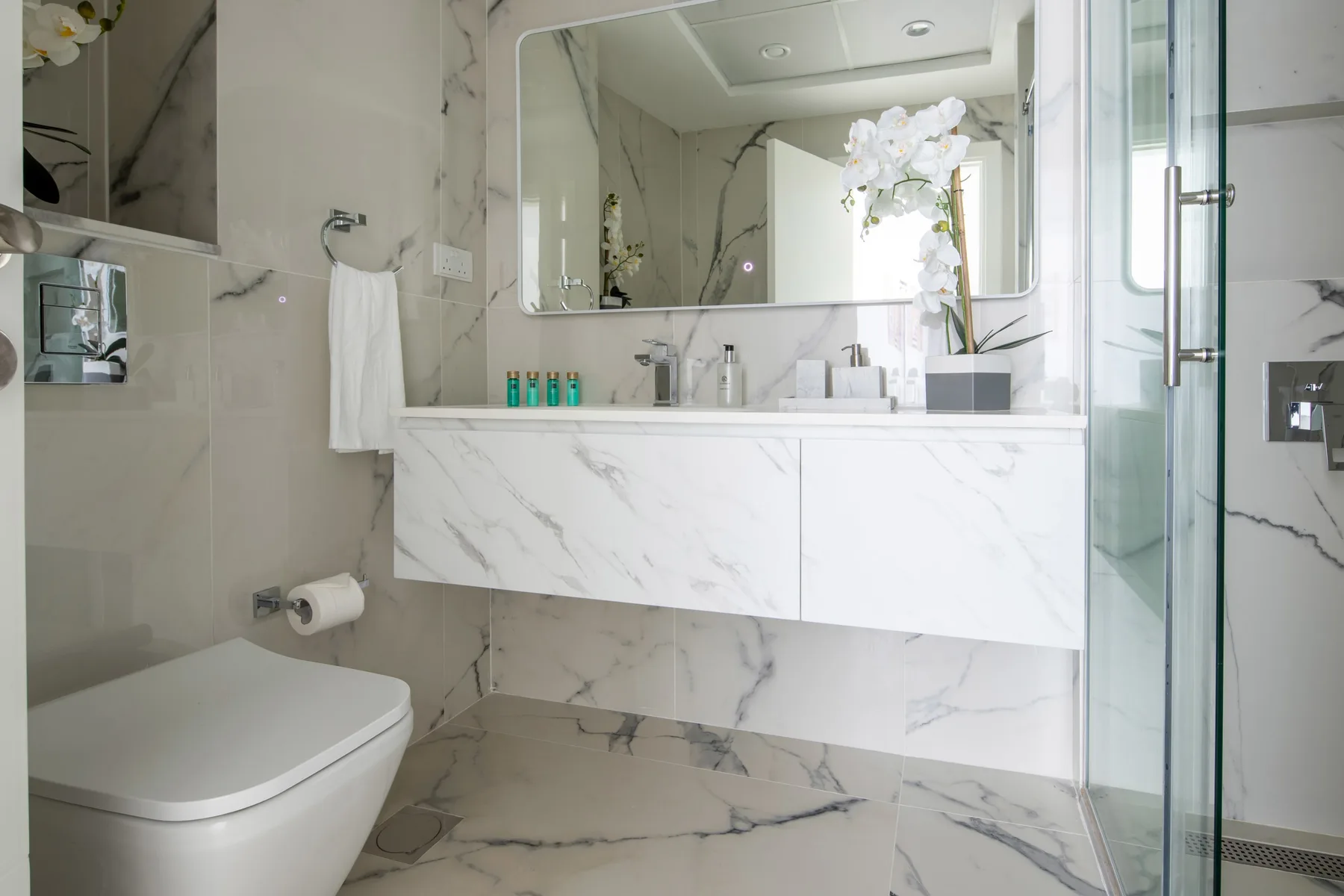A bright bathroom with a floating vanity, mirror, and glass shower.