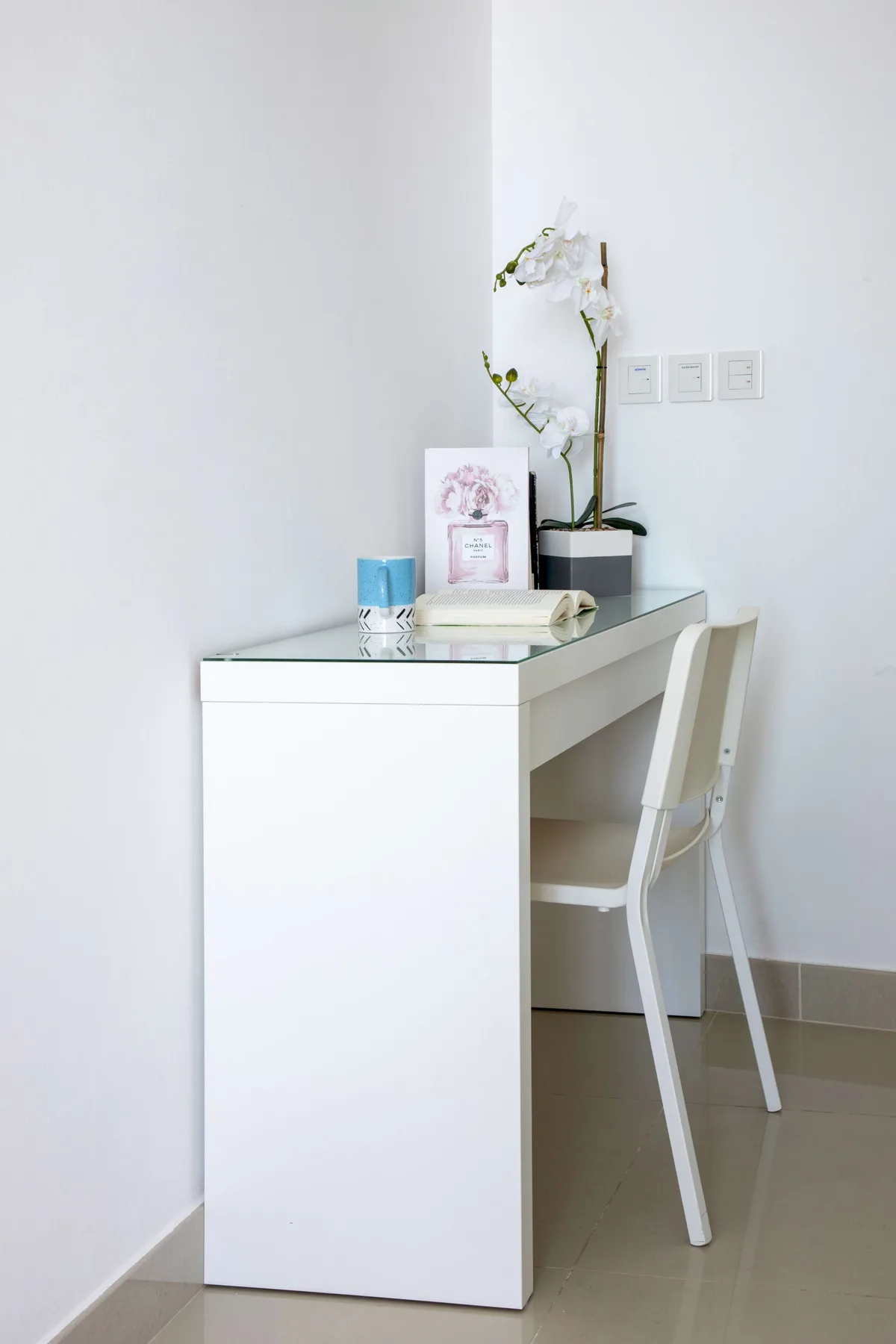 A white desk and chair sit against a wall, with an orchid on the desk.